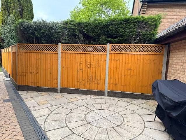Honey-stained wood fence panels with lattice tops and concrete posts behind a gray patio laid in a circle pattern